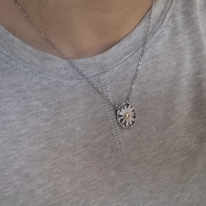 Close-up of a silver necklace featuring an oval daisy pendant with sparkling zircons