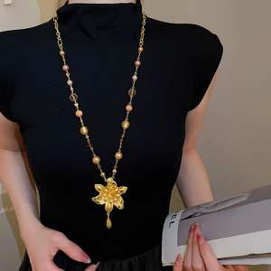 Détail d'un long collier doré avec pendentif fleur et perles colorées sur haut noir