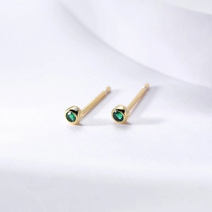 Detailed macro view of gold bezel-set round emerald green zircon stud earrings on white fabric
