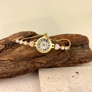 Détail d'une montre à quartz dorée avec bracelet en forme de cœur et cadran romain