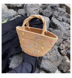 Close-up of handmade straw bucket bag with colorful pom-poms on a grey stone backdrop