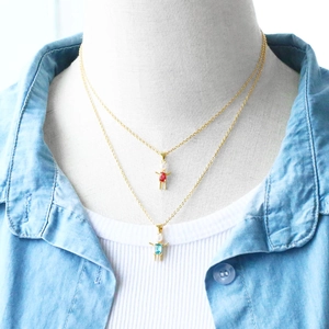 Detail of gold figure pendants with ruby and blue stones on model wearing denim shirt
