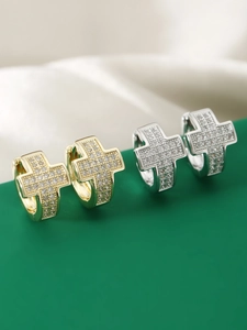 Close-up of gold and silver cross hoop earrings with pavé-set zircons on green surface
