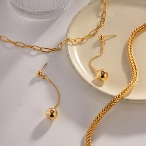 Detail of 18K gold-plated stainless steel ball earrings and necklaces on white tray
