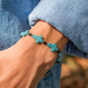 Men's turquoise cross bead bracelet with silver accents worn with denim jacket