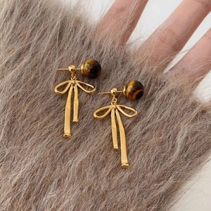 Elegant gold bow earrings with brown tiger eye beads on a soft grey faux fur surface