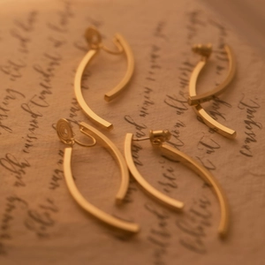 Detail of four gold curved long earrings displayed on a vintage handwritten paper background