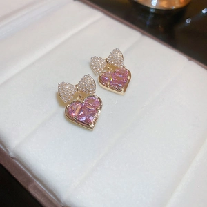 Macro detail of gold plated bow earrings featuring white pearls and a pink heart zircon