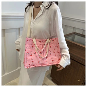 Pink shoulder bag with red cherry patterns and front pockets shown on a person