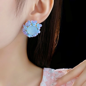 Close-up of elegant blue rose flower earrings with translucent central stone on model