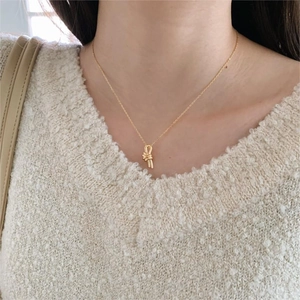 Close-up of a minimalist golden knotted pendant necklace worn on a beige sweater