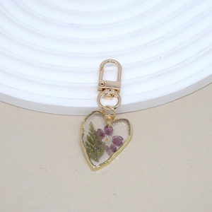 Handmade heart resin keychain with purple dried flowers and gold foil on white plate