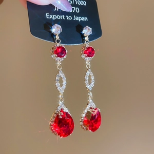 Macro shot of gold-plated drop earrings with red gemstones and sparkling rhinestones
