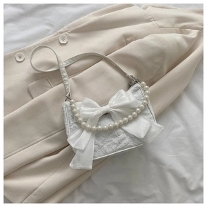 Close-up of a white textured shoulder bag featuring a large bow and pearl chain details