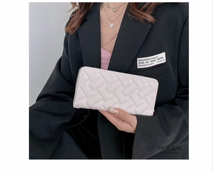 Detail of a beige embossed long wallet with a zip closure held by a model in a black suit