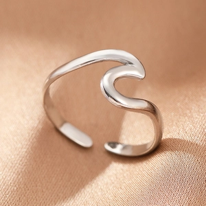 Macro view of a wavy silver stainless steel open ring on soft champagne satin fabric