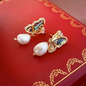 Golden butterfly earrings with abalone shell wings and baroque pearls on red jewelry box