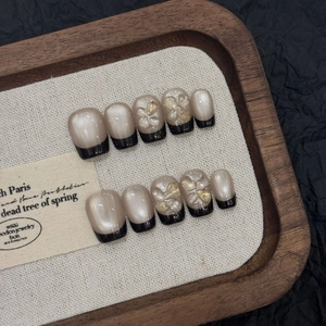 Detail of handmade black French cat-eye press-on nails with 3D floral accents on wood