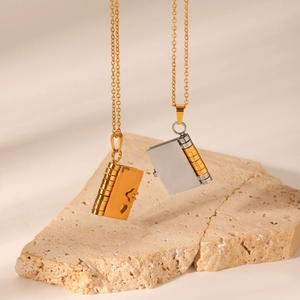 Detail of book-shaped heart locket necklaces on a rock, showing fine metallic texture