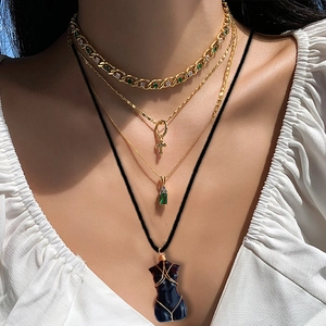Layered gold necklace featuring green crystal pendants and a female body torso charm