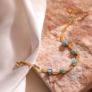 Goldenes Schlangenarmband mit fünf türkisfarbenen Wassertropfen auf Seide und Stein