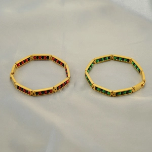 Detail view of gold titanium beaded bracelets with red and green charms on silk fabric