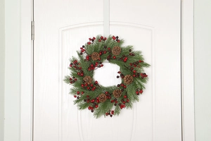 Detail of Christmas wreath with red berries and pine cones on a white door