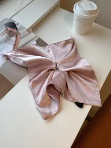 Detail of pink satin scarf scrunchie with neat edges and handmade label on white desk