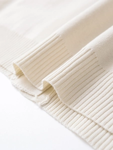 Detailed close-up of cream knit sweater showing fine ribbed cuffs and fabric texture