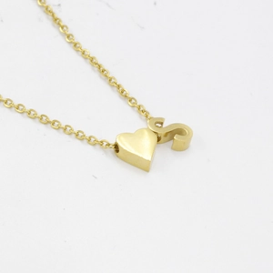 Detail of gold heart pendant and letter S charm on mirror finish stainless steel necklace