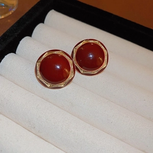 Dettaglio di orecchini circolari rosso scuro con bordi esagonali dorati su velluto