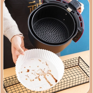 White round air fryer paper liner showing oil resistance after cooking in a black basket