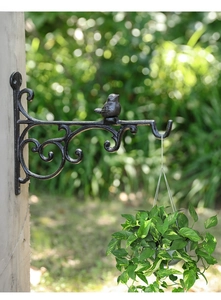 Detail einer Wandhalterung aus Gusseisen mit Vogelmotiv und hängender Pflanze