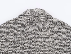 Gros plan sur la texture à chevrons d'un manteau en laine noir et blanc montrant le tissage