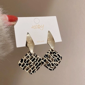 Close-up of geometric drop earrings featuring 925 silver posts and black white checkered patterns