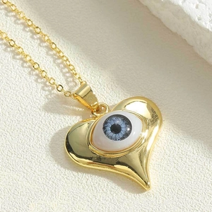 Macro detail of gold heart pendant featuring a blue evil eye on polished chain