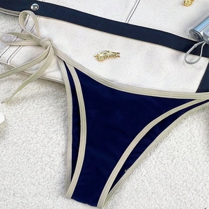 Detail of navy blue bikini bottom with side ties and a gold metal wing charm detail