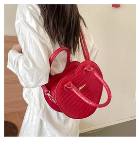 Vue détaillée d'un sac à main rouge en forme de cœur avec motif crocodile à l'épaule