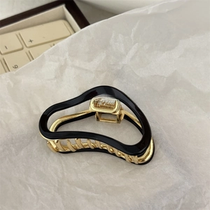 Detail view of the wave-shaped golden metal hair claw clip with black finish