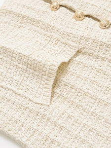 Detailed macro view of gold embossed lion buttons on a cream knit tweed cardigan