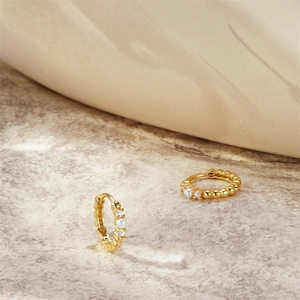 Macro view of gold hoop earrings with white pearls and zircons on marble surface