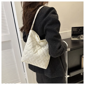 Detail of white heart-quilted puffer tote bag with gold snap button and soft texture