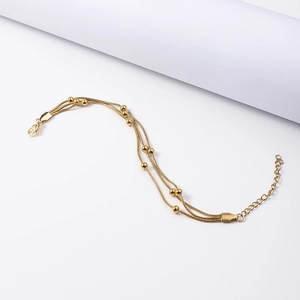 Detailed macro view of triple-layered gold snake chain bracelet with small golden beads