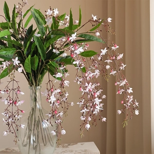 Artificial drooping jasmine branches with white and pink flowers in a glass vase