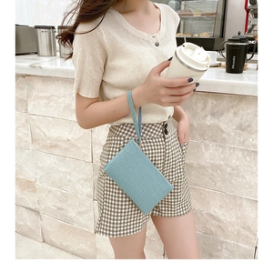 Close-up of a light blue crocodile pattern wristlet bag held by a model in a cafe setting