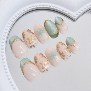 Press on nails with green cat eye effect, golden floral art, and nude pink tones
