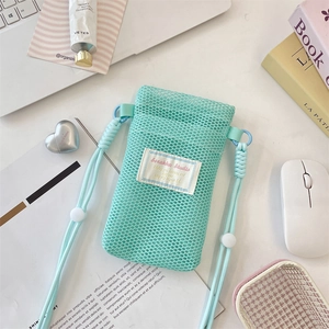 Close-up of mint green mesh phone bag with adjustable rope strap on a lifestyle desk setup