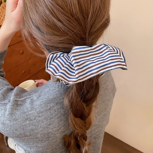 Gros plan d'une pince à cheveux en tissu rayé en forme de nœud sur cheveux bruns