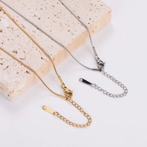 Close-up of gold and silver snake chain necklaces with lobster clasps on stone