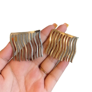 Hand hält silberne und goldene gewellte Metall-Haarkämme mit poliertem Metall-Finish